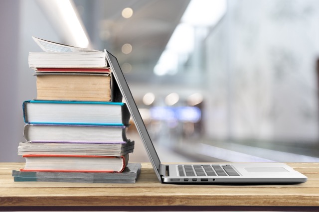 A laptop put against a stack of books