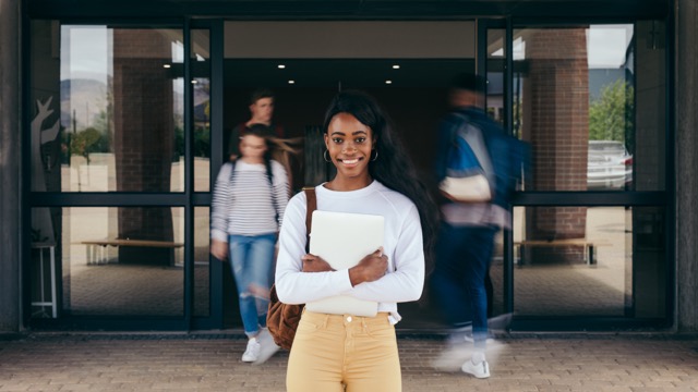 Student standing and smiling, holding a book