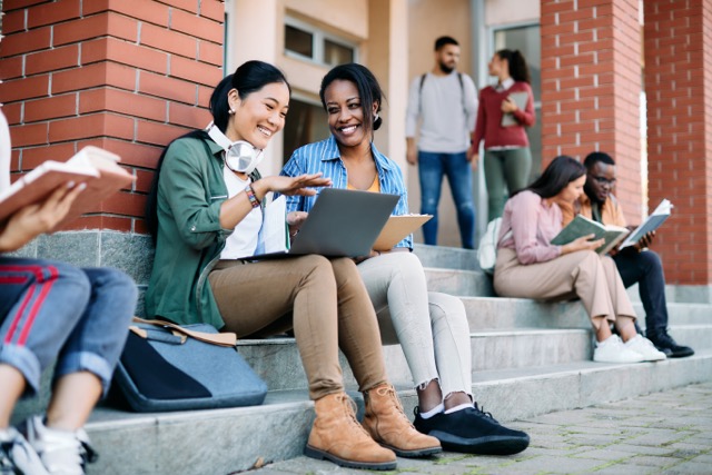 Two female students sitting on campus  stairs and discussing student life.