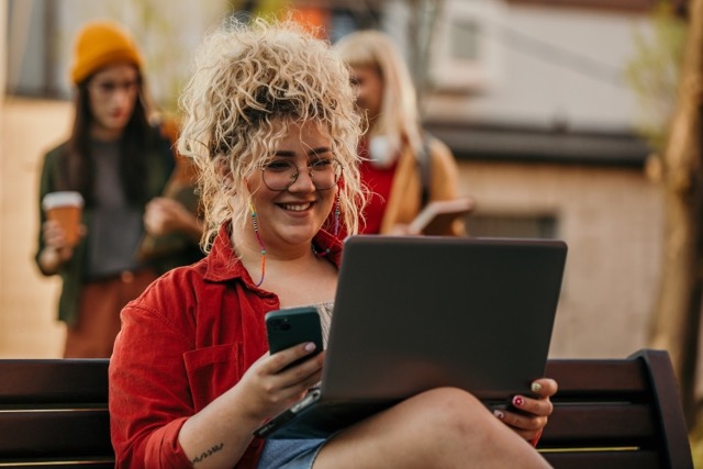 Girl carrying phone and laptop smiling