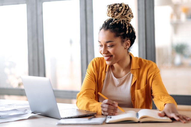 Girl wearing an orange shirt with braids smiling at laptop