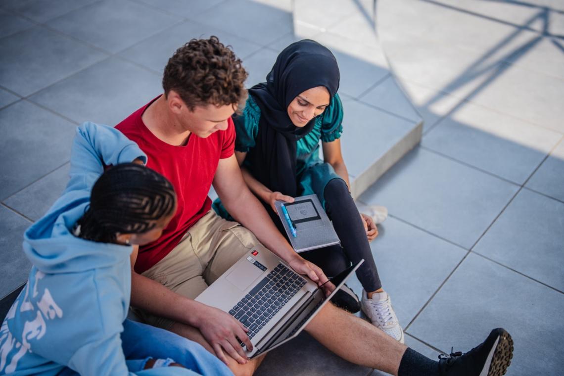 three students sitting and looking at one laptop