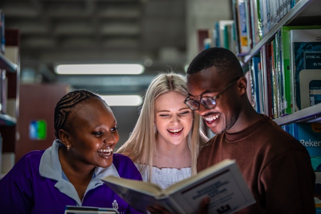 Group of students at the library reading a book and laughing
