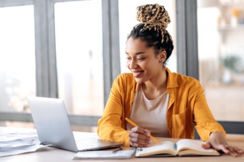 Girl wearing an orange shirt with braids smiling at laptop