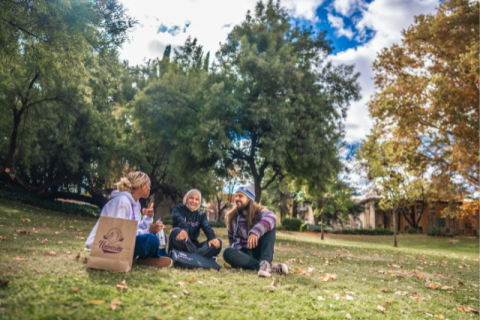 Two female and one male students sitting on the campus park, conversing.