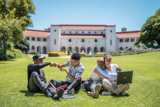 Four students sitting by the lawn interacting